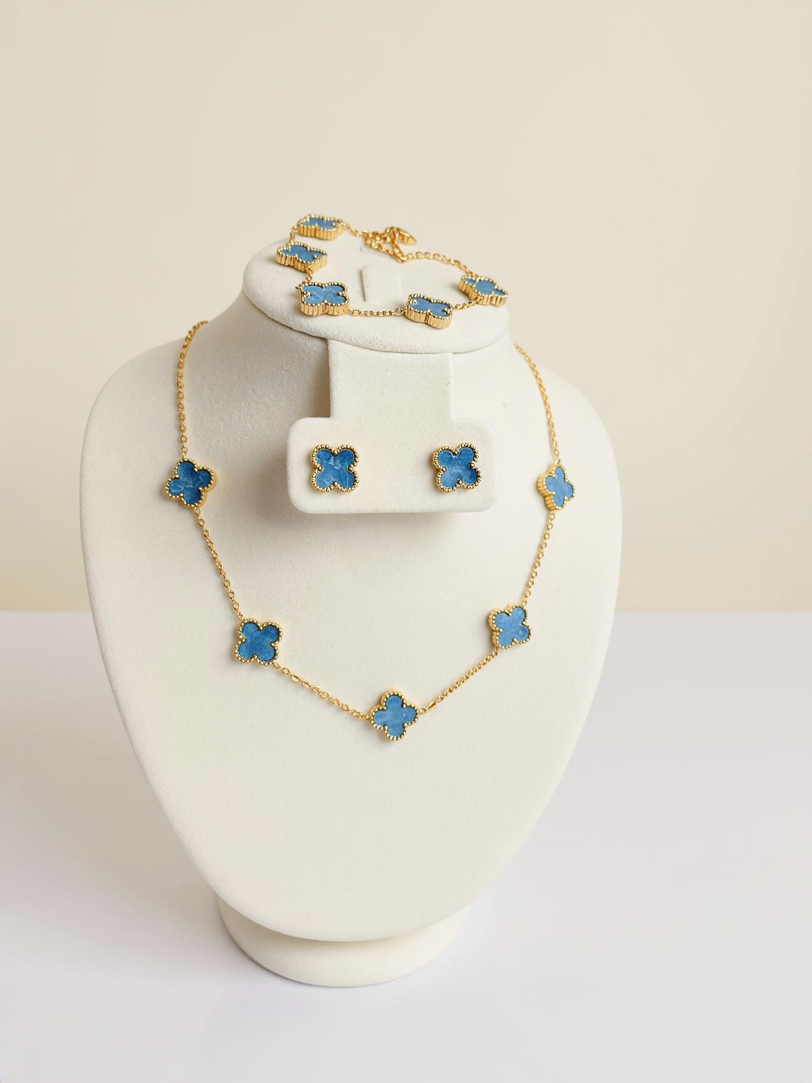 Blue five-clover necklace with matching earrings and bracelet on a white display.