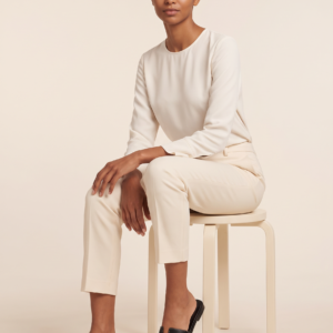 Seated model wearing black cutout slide sandals with an ivory blouse and cream trousers.